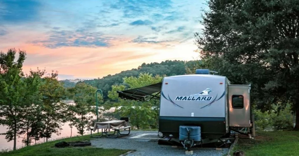 Travel trailer by lakeside at sunset.