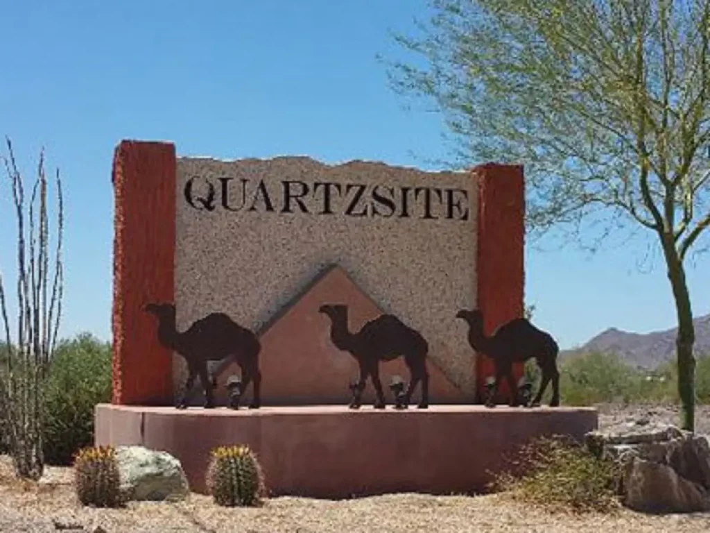 Quartzsite town sign with camel silhouettes and desert backdrop.