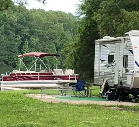 RV and pontoon boat at lakeside campsite.
